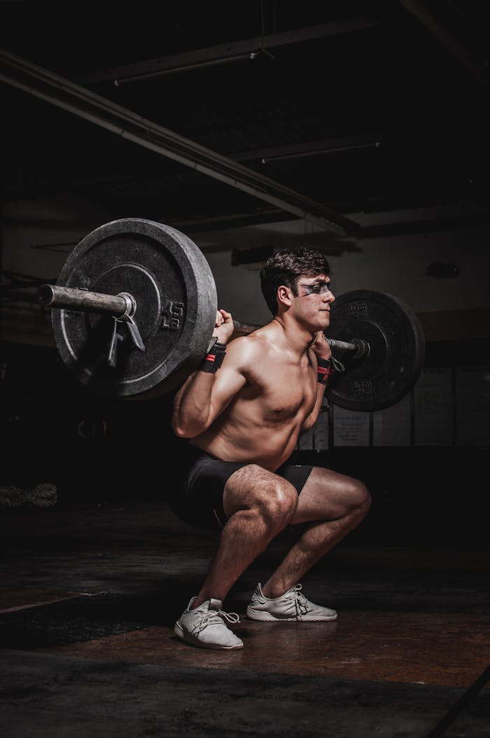 why-choose-us Shirtless man performing a barbell squat, showcasing strength and fitness.