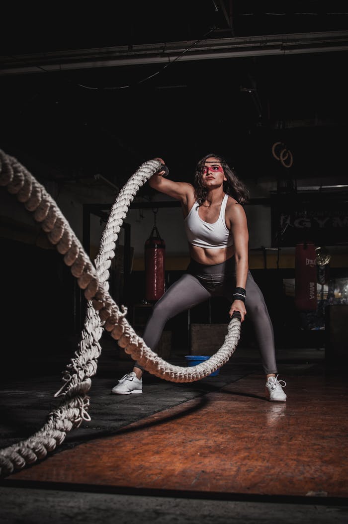 our-services-3 Female athlete demonstrating strength with battle ropes in a gym.