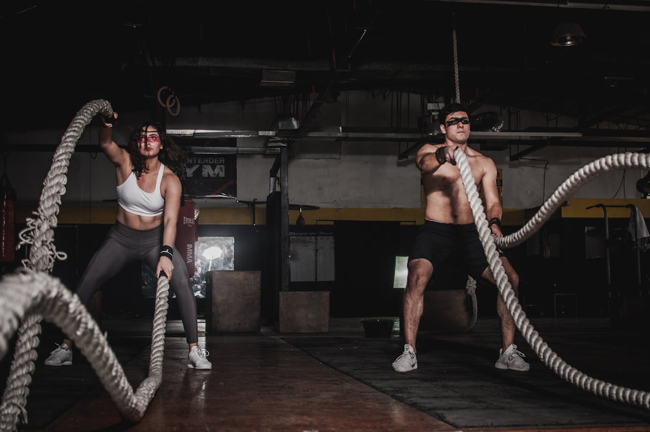 about-01 Two people engage in a powerful indoor battle rope workout, showcasing strength and energy.