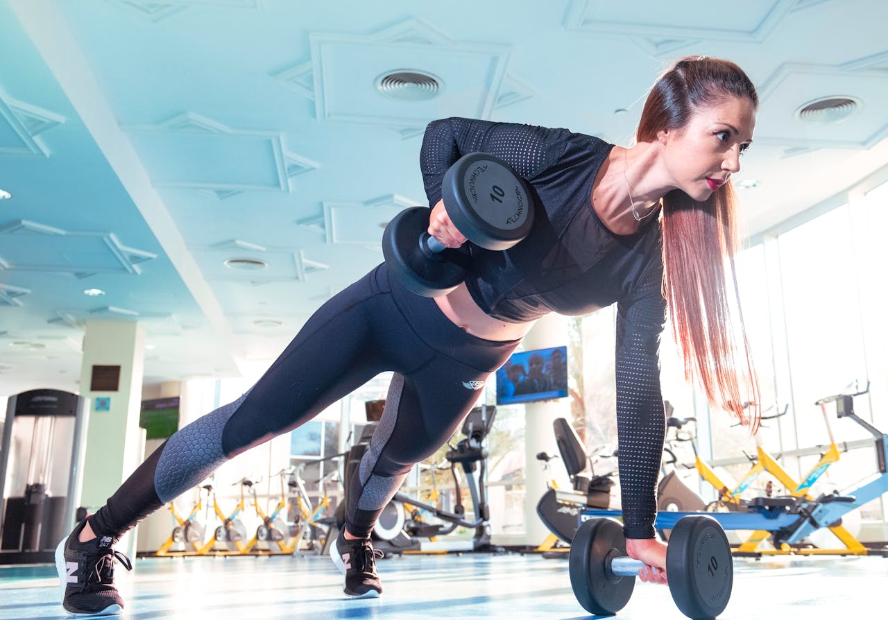 gallery-1 Woman performing a plank row with dumbbells in a bright Dubai gym.